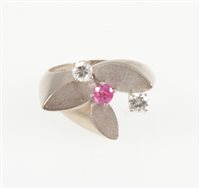 Lot 221 - A contemporary ruby and diamond dress ring, two brilliant cut diamonds and a single pink ruby claw set on a white metal floral mount with three satin finish petals, shank marked 585