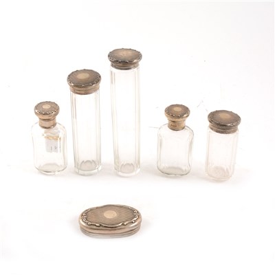 Lot 246 - Five silver capped dressing table set bottles and a matching lid by Adie Brothers Ltd, engine-turned with vacant centre circular cartouche, scroll and fleur-de-lys border, Birmingham 1923