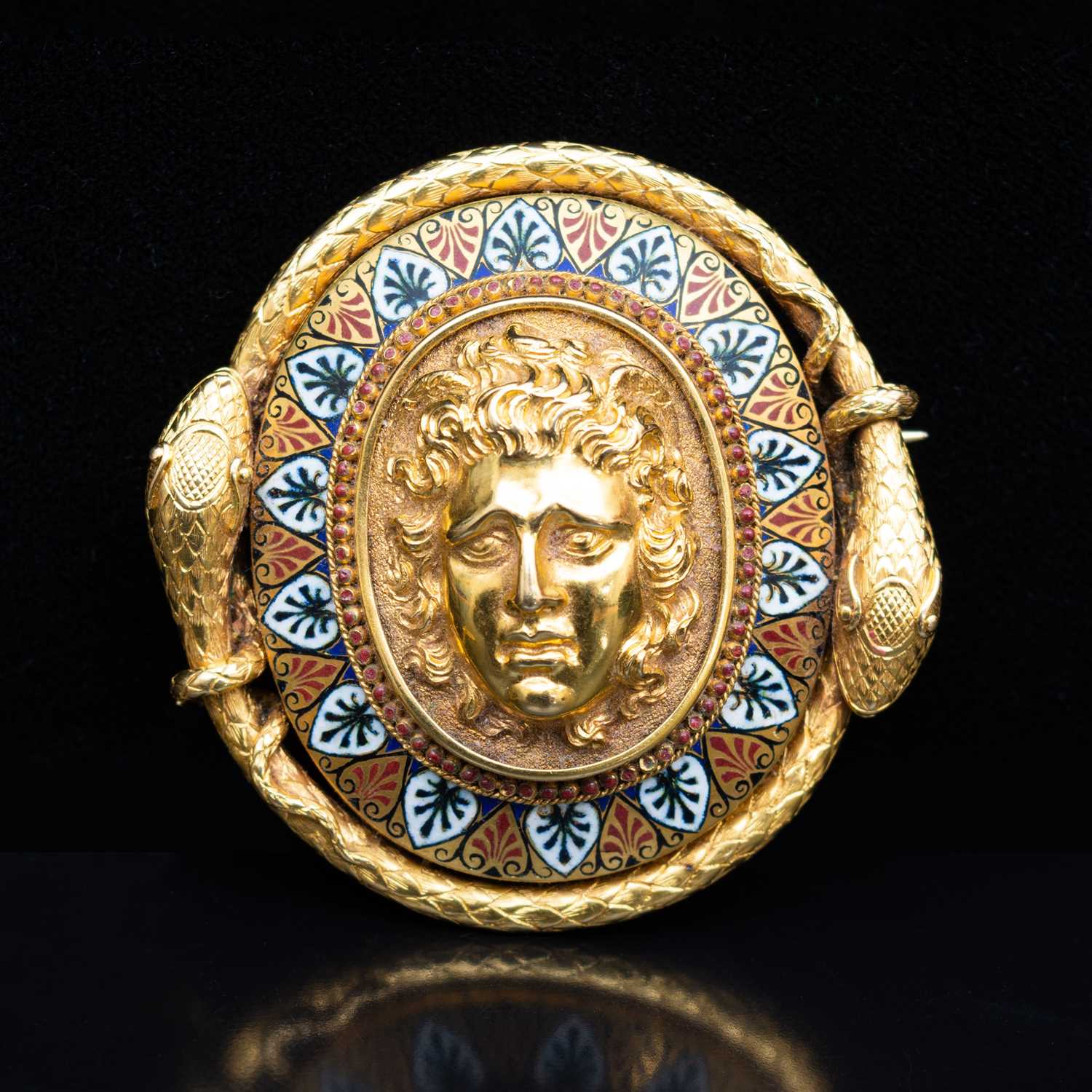 69 - A late 19th Century yellow metal and enamel oval brooch, with a central mask in high relief.