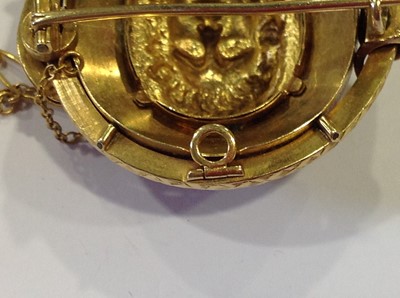 Lot 69 - A late 19th Century yellow metal and enamel oval brooch, with a central mask in high relief.